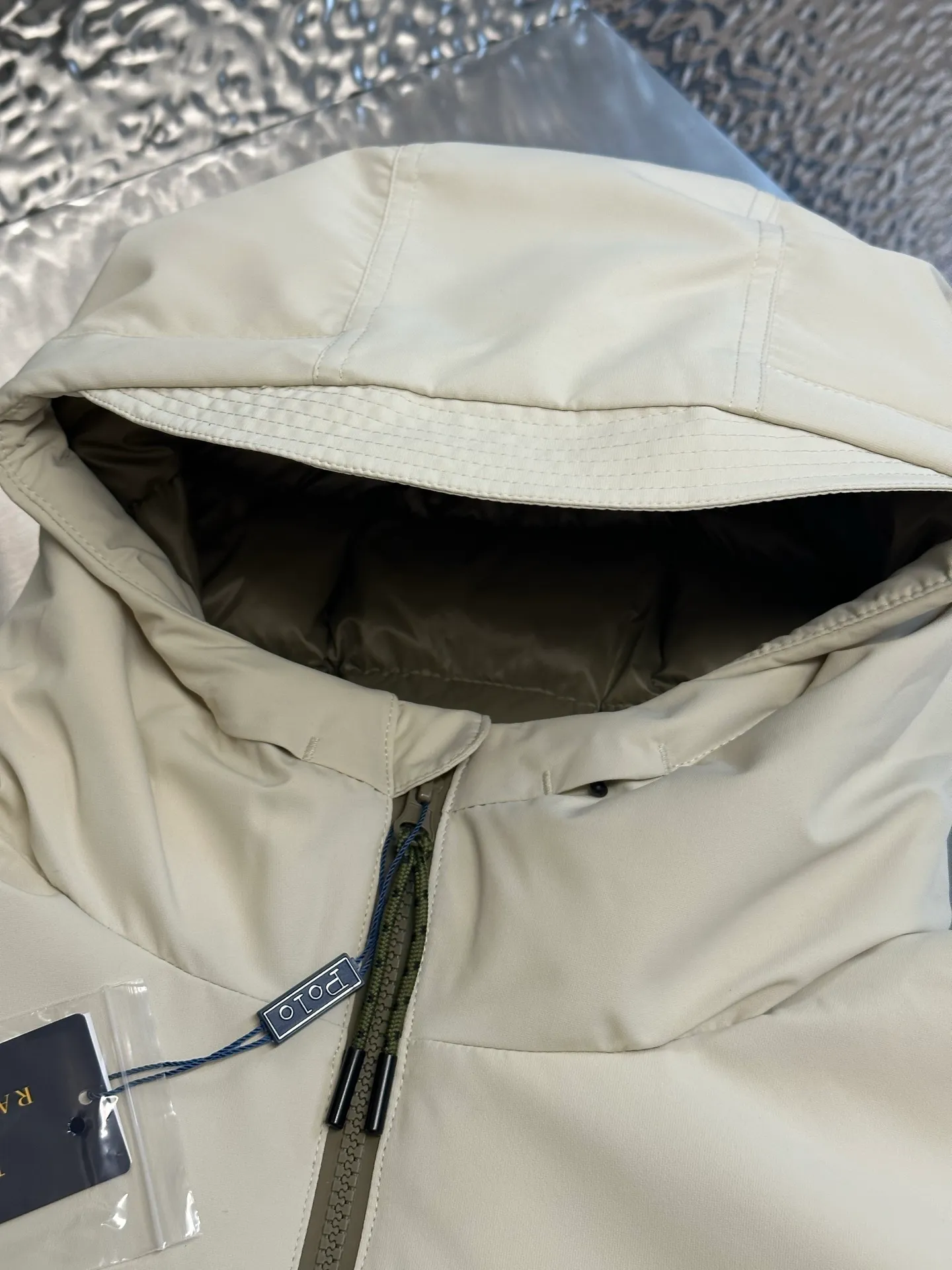 P970 Ralph Lauren logo hooded down jacket. The density of high-density nylon taffeta is about 210T-300T. The surface is smooth and slightly matte. It has excellent windproof and waterproof performance (with DWR water-repellent treatment). It has strong wrinkle resistance and is easy to care for. It is in line with the positioning of American casual "durable and practical".  The inner lining is made of 100% polyamide. The high-density and tight weaving process prevents fine lint from getting out of the gaps in the fabric. The smooth surface improves the putting on and taking off experience, and the excellent wear and tear resistance ensures damage caused by frequent use, while the light and soft texture does not affect the overall weight.  It uses 90 white duck down with a weight of 220g to ensure excellent thermal insulation performance. After strict screening and processing, the velvet is not easily drilled, ensuring durability. The classic jacket has a slightly loose fit, with slightly dropped shoulder lines (the shoulder width is 1-2cm wider than the standard fit). The length reaches the hips, and the sleeves are slightly tapered straight sleeves, taking into account freedom of movement and casual style.  The adjustable Velcro on the cuffs allows you to freely adjust the tightness according to the thickness of your wrist and personal preferences, effectively preventing cold wind from intruding, and improving the warmth performance. Two zippered pockets on the front are convenient for placing frequently used items, and the zipper design ensures that items are not easily lost. A built-in pocket on the left side of the chest provides a safe storage space for some small private items.  The drawstring design at the hem allows you to adjust the shape of the jacket according to your body shape and dressing needs. Whether it is loose and casual or slim and neat, you can easily control it.  Polo horse logo on the left chest: flat satin stitch embroidery (satin embroidery), using 100% polyester high color fastness embroidery thread (the color number is consistent with the brand's standard red color card), the stitch density is 12-15 stitches/cm, the outline of the horse logo is clear, and the details of the rider and horse are burr-free. Precise positioning through the template (12cm from the bottom of the collar and 8cm from the placket) ensures symmetry and centering.  size：s m l xl